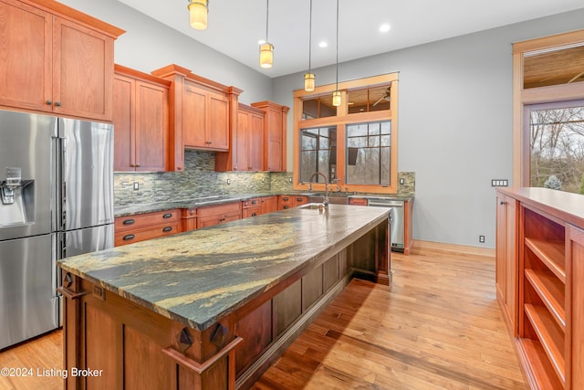 kitchen featuring light wood-type flooring, tasteful backsplash, dark stone counters, stainless steel appliances, and a center island with sink