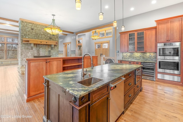 kitchen featuring sink, stainless steel appliances, light hardwood / wood-style flooring, decorative light fixtures, and a kitchen island with sink