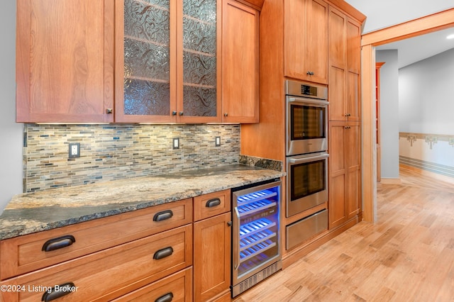 kitchen featuring beverage cooler, tasteful backsplash, double oven, stone countertops, and light wood-type flooring