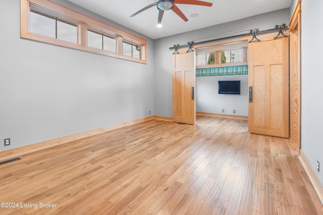 interior space featuring light wood-type flooring, ceiling fan, and a barn door