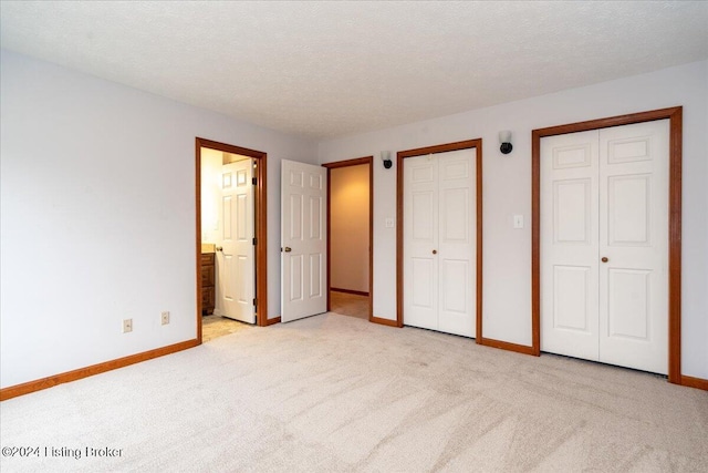 unfurnished bedroom with a textured ceiling, light colored carpet, ensuite bath, and multiple closets