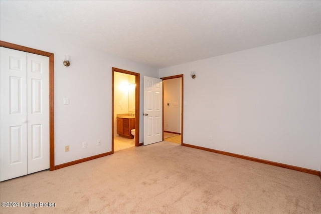 unfurnished bedroom with ensuite bath, light carpet, and a closet