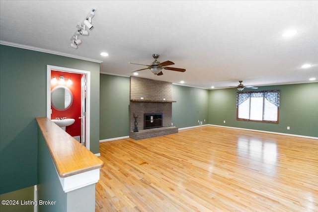 unfurnished living room featuring hardwood / wood-style floors, ceiling fan, crown molding, and a fireplace