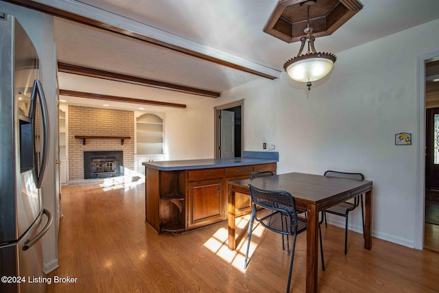 dining room with beam ceiling, built in shelves, light hardwood / wood-style floors, and a brick fireplace