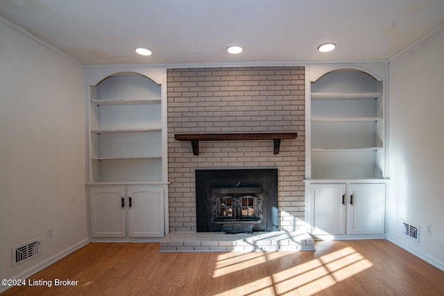 unfurnished living room with built in shelves, light wood-type flooring, and crown molding