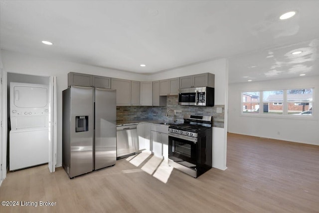 kitchen with stainless steel appliances, tasteful backsplash, light hardwood / wood-style flooring, stacked washer / dryer, and gray cabinets