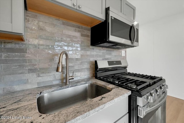 kitchen with light stone countertops, stainless steel appliances, tasteful backsplash, and sink