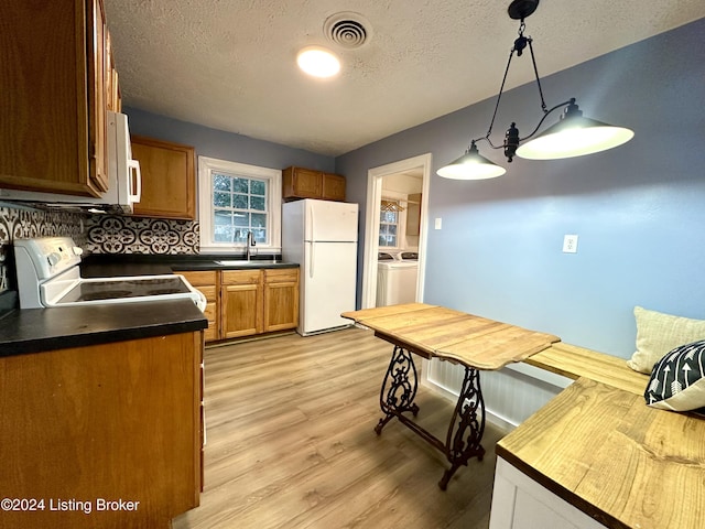 kitchen with sink, hanging light fixtures, white appliances, washer and clothes dryer, and light wood-type flooring