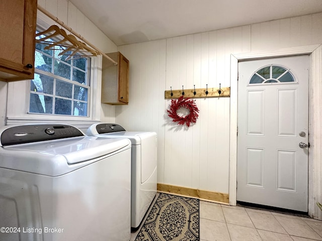 clothes washing area featuring wooden walls, light tile patterned flooring, cabinets, and washing machine and dryer