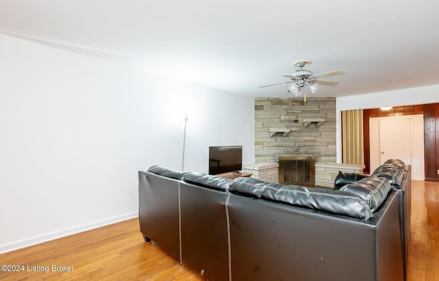 living room with light hardwood / wood-style flooring, ceiling fan, and a stone fireplace