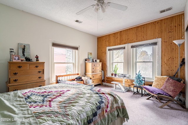 carpeted bedroom with ceiling fan, a textured ceiling, and wooden walls