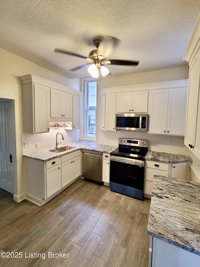 kitchen featuring white cabinets, sink, light wood-type flooring, light stone countertops, and appliances with stainless steel finishes