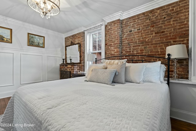 bedroom with dark wood-type flooring, crown molding, a fireplace, a notable chandelier, and brick wall