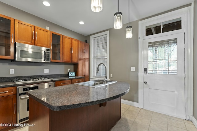 kitchen with stainless steel appliances, a kitchen island with sink, sink, pendant lighting, and light tile patterned floors