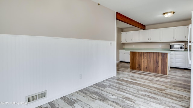 kitchen with beam ceiling, a kitchen island, white cabinets, and light wood-type flooring