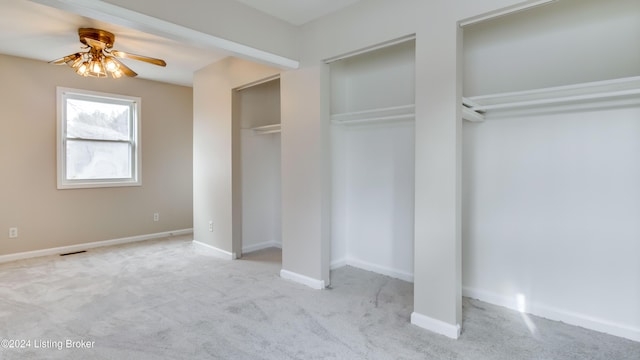 unfurnished bedroom featuring ceiling fan, light colored carpet, and two closets