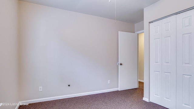 unfurnished bedroom with dark colored carpet and a closet