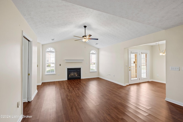 unfurnished living room featuring plenty of natural light, dark wood-type flooring, ceiling fan with notable chandelier, and vaulted ceiling