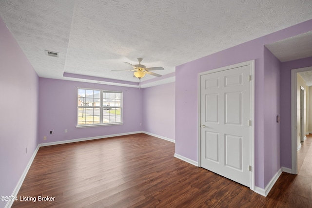 unfurnished room featuring a textured ceiling, dark hardwood / wood-style flooring, a raised ceiling, and ceiling fan