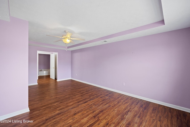 spare room featuring a raised ceiling, ceiling fan, dark hardwood / wood-style flooring, and a textured ceiling