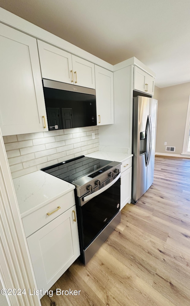 kitchen with backsplash, white cabinets, light stone countertops, light wood-type flooring, and stainless steel appliances