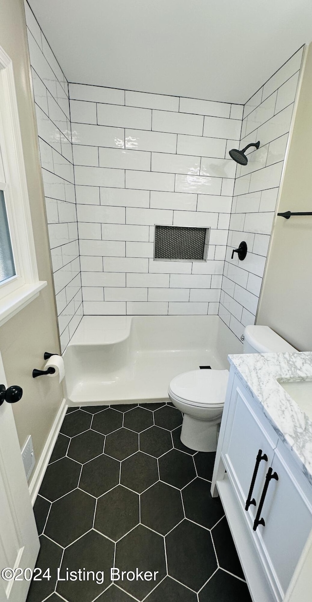 bathroom with tile patterned floors, toilet, vanity, and tiled shower