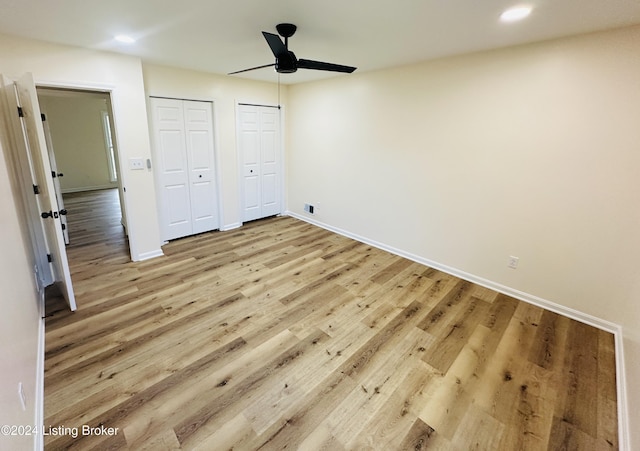 unfurnished bedroom featuring hardwood / wood-style flooring, ceiling fan, and multiple closets