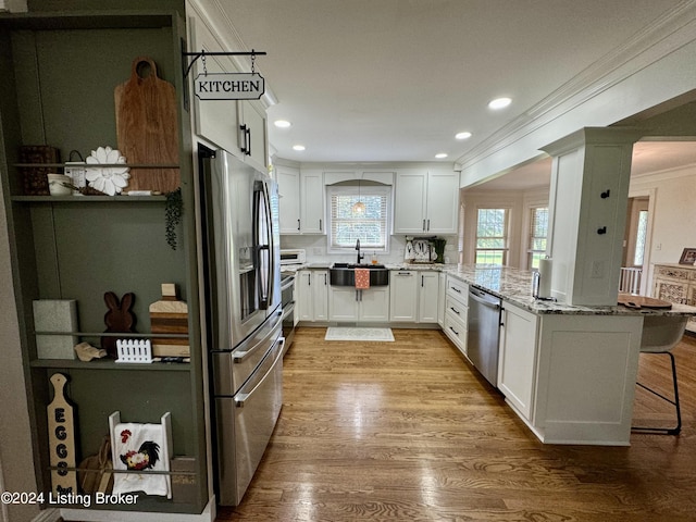 kitchen featuring white cabinetry, stainless steel appliances, light stone counters, light hardwood / wood-style floors, and a kitchen bar