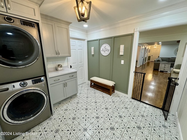 clothes washing area with stacked washer / drying machine, cabinets, and ornamental molding