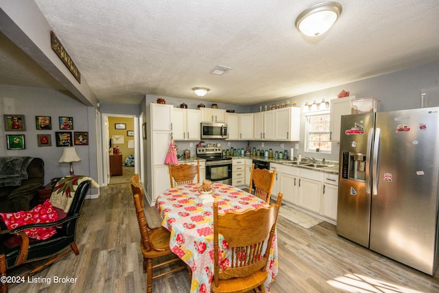 kitchen featuring a textured ceiling, white cabinetry, stainless steel appliances, and light hardwood / wood-style flooring