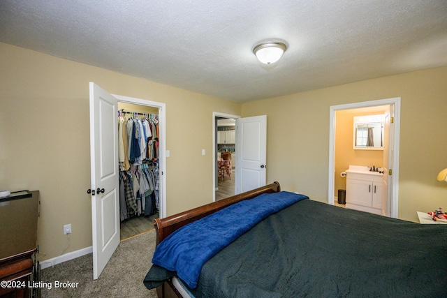 bedroom with carpet flooring, a textured ceiling, ensuite bath, and a closet