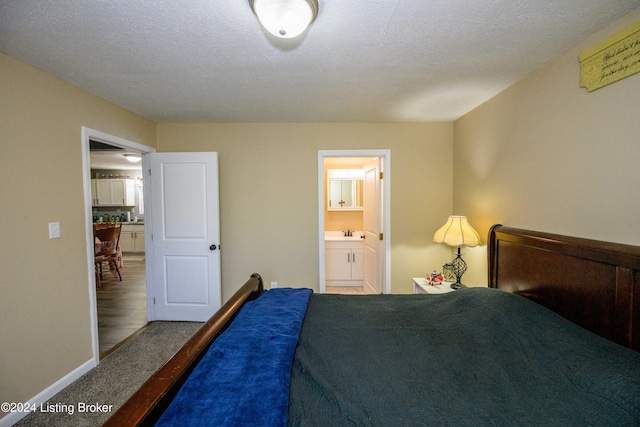 carpeted bedroom with sink, a textured ceiling, and ensuite bath