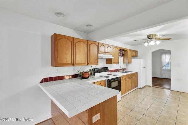 kitchen with electric stove, sink, tile counters, kitchen peninsula, and white fridge