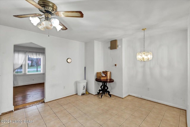 tiled spare room featuring ceiling fan with notable chandelier