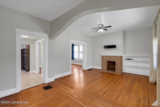 unfurnished living room featuring ceiling fan, a tiled fireplace, and light hardwood / wood-style flooring