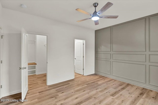 unfurnished bedroom with ceiling fan, a walk in closet, and light wood-type flooring