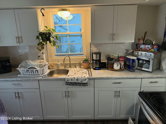 kitchen featuring electric range, white cabinetry, sink, and tasteful backsplash