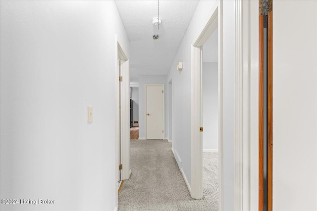 corridor with light colored carpet and a textured ceiling