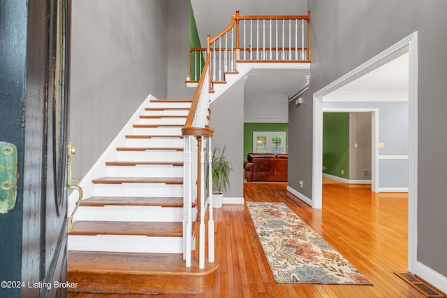 staircase with wood-type flooring, a high ceiling, and ornamental molding