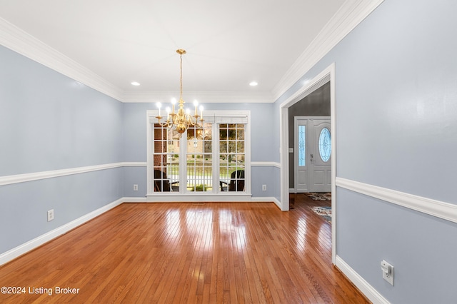 unfurnished dining area with hardwood / wood-style floors, crown molding, and a notable chandelier