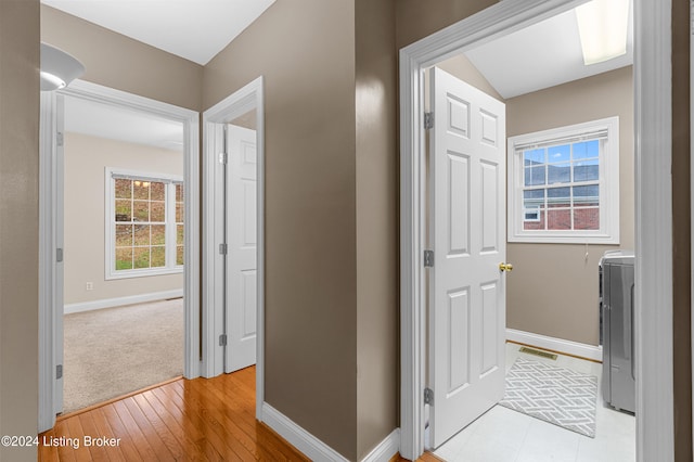 hall featuring washer / dryer, vaulted ceiling, light hardwood / wood-style flooring, and a healthy amount of sunlight