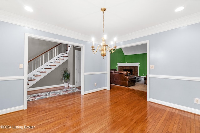 unfurnished dining area featuring a fireplace, crown molding, hardwood / wood-style floors, and an inviting chandelier