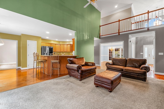 living room with ceiling fan, ornamental molding, a high ceiling, and light hardwood / wood-style flooring