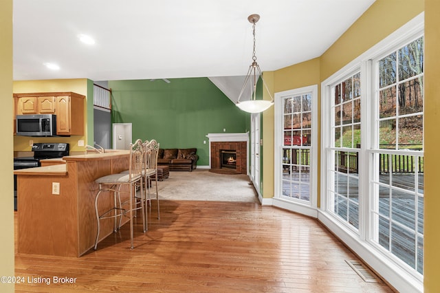 kitchen with hanging light fixtures, light hardwood / wood-style flooring, a fireplace, black range with electric cooktop, and a breakfast bar area