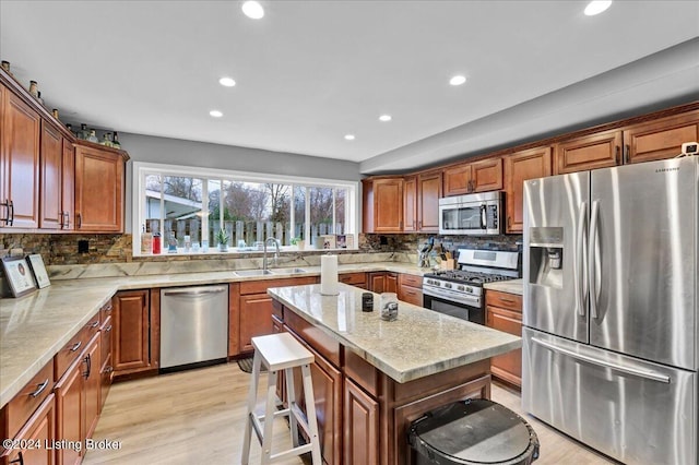 kitchen featuring sink, light hardwood / wood-style floors, a kitchen bar, a kitchen island, and appliances with stainless steel finishes