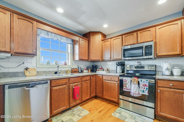 kitchen featuring appliances with stainless steel finishes, backsplash, light hardwood / wood-style flooring, and sink