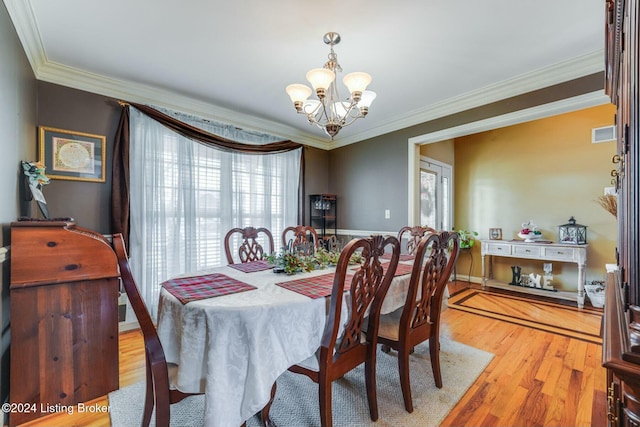 dining area featuring light hardwood / wood-style floors, crown molding, and an inviting chandelier