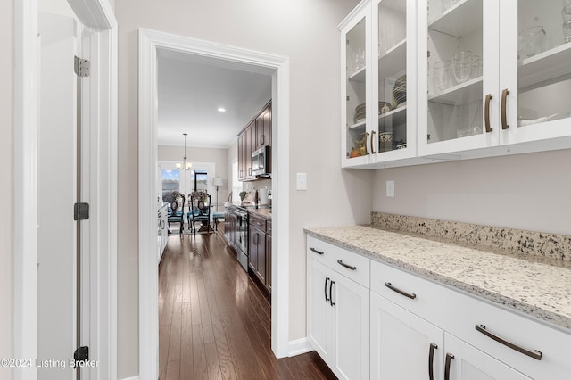 bar with dark hardwood / wood-style flooring, stainless steel appliances, white cabinetry, and light stone counters