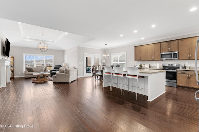 kitchen with appliances with stainless steel finishes, dark hardwood / wood-style flooring, a notable chandelier, a breakfast bar area, and an island with sink