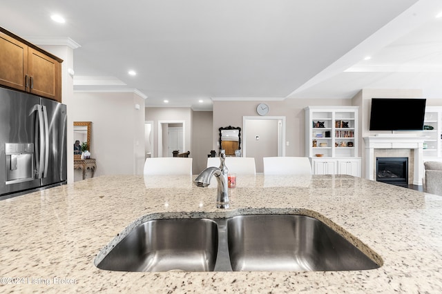 kitchen with a tiled fireplace, stainless steel fridge with ice dispenser, sink, and light stone countertops